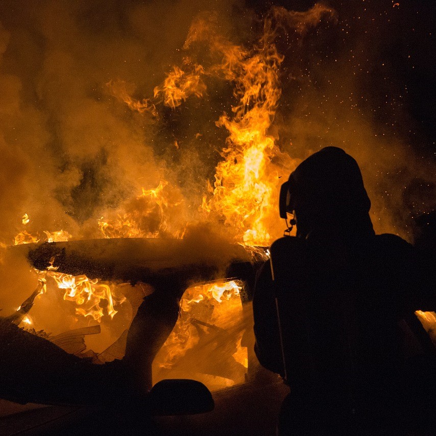 Silhouette of a Firefighter Fighting a Vehicle Fire Among Large Orange Flames and Smoke